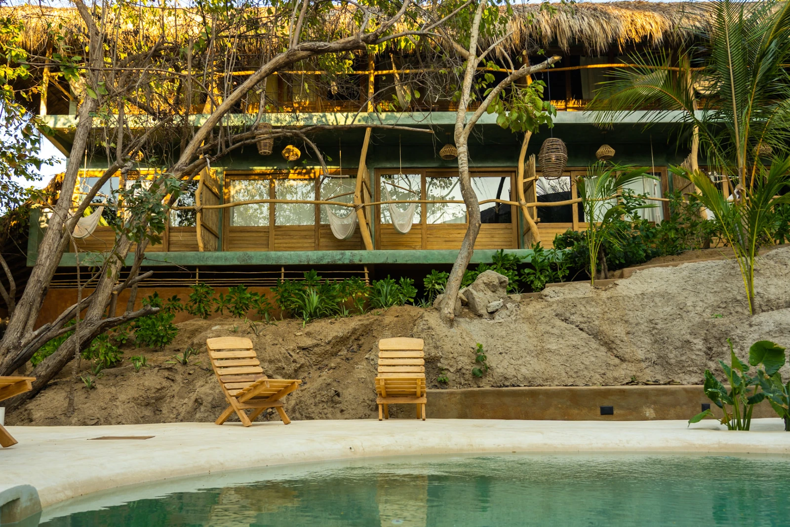 Alberca y camastros para asolearse entre palmeras y jardín tropical en Cocos Hotel Zipolite